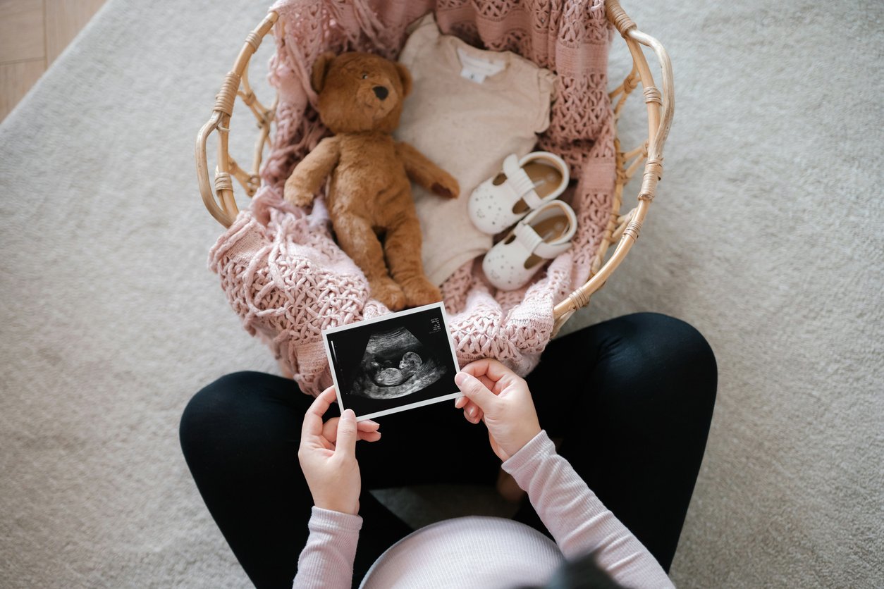 Gestante segurando ultrassom em frente a cestinho de bebe